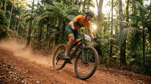 XCO racer in Australian green and gold lycra climbing a red dirt fire road through Queensland rainforest at golden hour