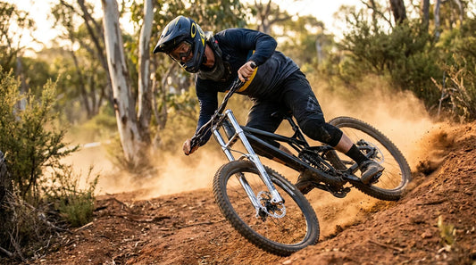 Downhill mountain bike racer in dark navy and yellow race kit ripping a dusty berm on a steep Australian DH track at golden hour