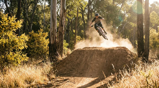 A mountain biker hitting a large dirt jump in an Australian bush setting at golden hour.