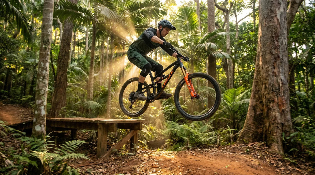 Mountain biker mid-air on a tabletop jump in a tropical north Queensland rainforest trail network at golden hour