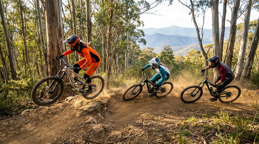 Three enduro riders in colourful kits ripping a fast bermed corner with the Victorian high country behind them