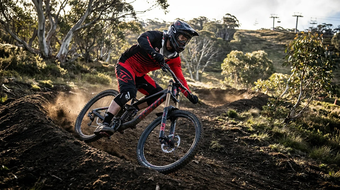 DH racer in black and red kit ripping a fresh dark-loam berm at Thredbo with chairlift towers in the background