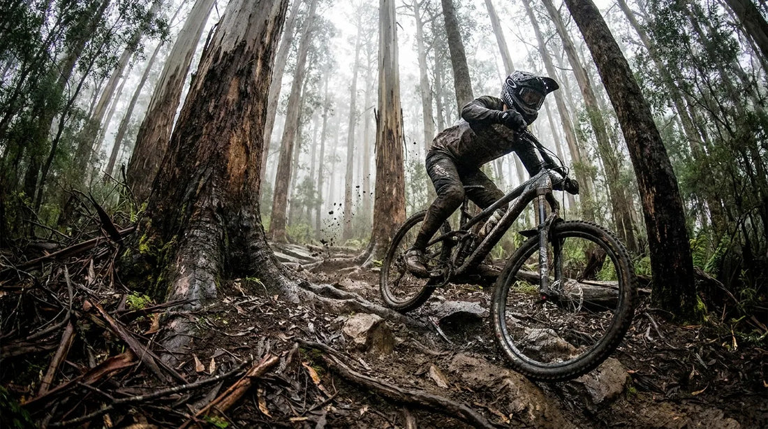 A mountain biker pinning a technical rock garden in a misty Tasmanian forest.