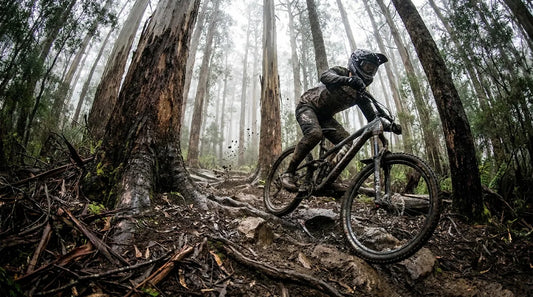A mountain biker pinning a technical rock garden in a misty Tasmanian forest.